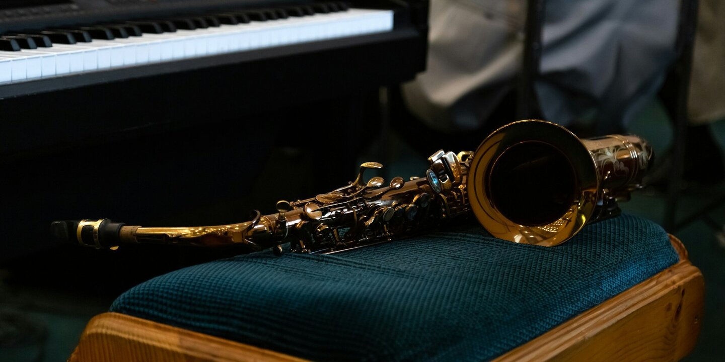Ein Saxophon liegt auf einer gepolsterten Bank vor einem E-Piano.